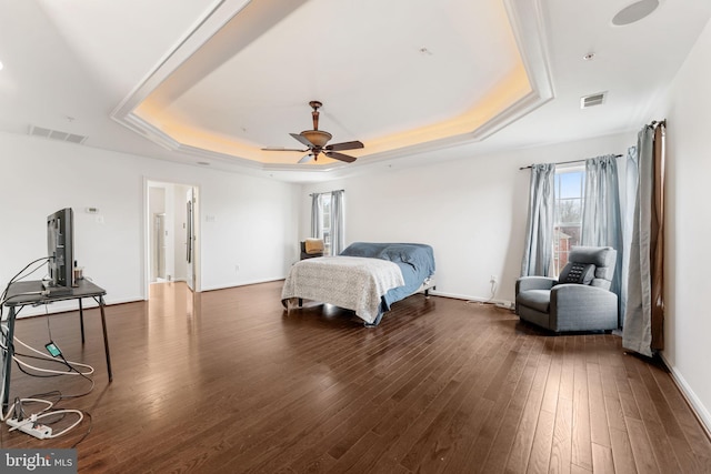 bedroom with dark wood-type flooring, ceiling fan, and a tray ceiling