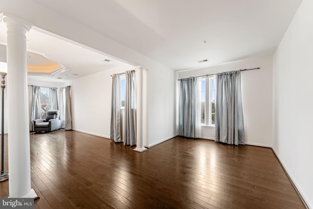 unfurnished room with ornate columns, a raised ceiling, and dark hardwood / wood-style floors