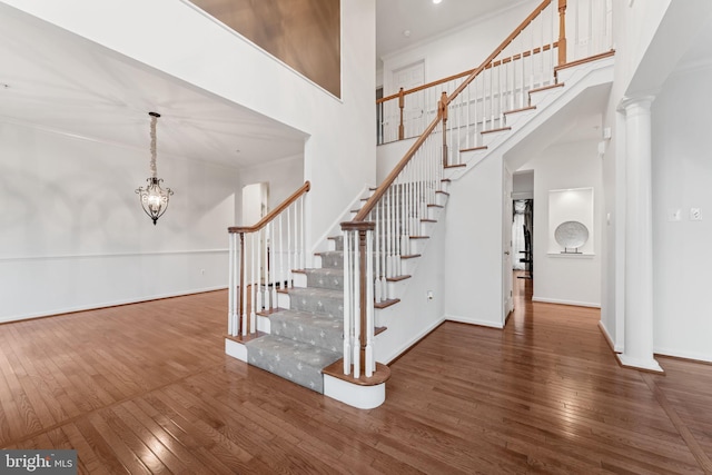 stairs with a notable chandelier, a towering ceiling, and wood-type flooring