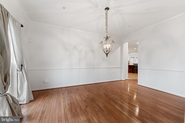 empty room featuring hardwood / wood-style flooring, ornamental molding, and a chandelier