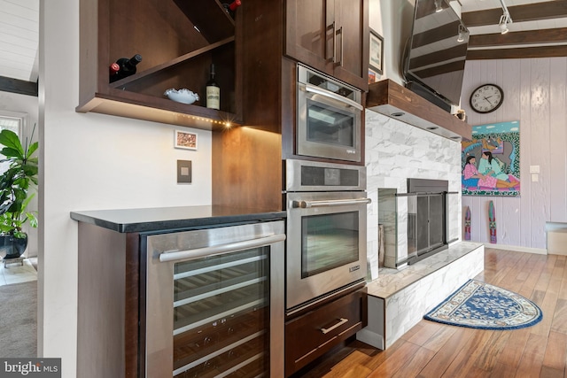 kitchen featuring wood walls, beverage cooler, oven, and light wood-type flooring