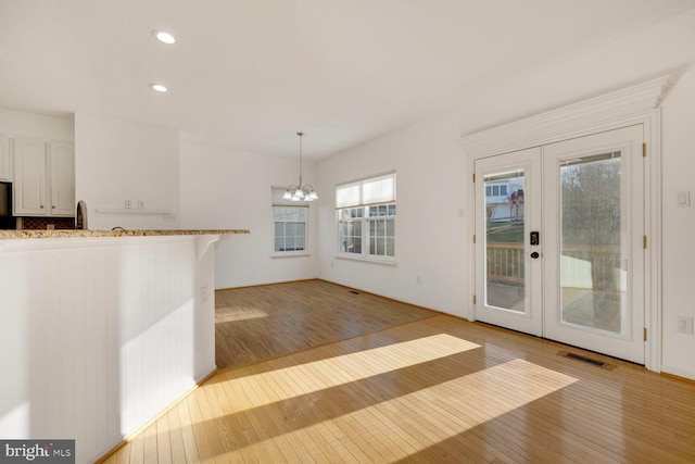 kitchen with white cabinetry, hanging light fixtures, a notable chandelier, and light hardwood / wood-style floors