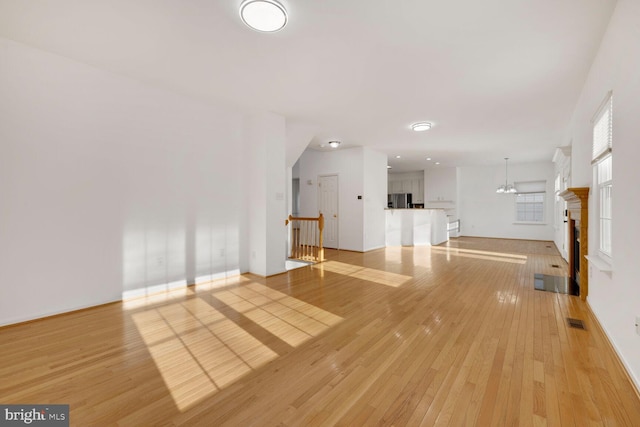 unfurnished living room with an inviting chandelier and light wood-type flooring