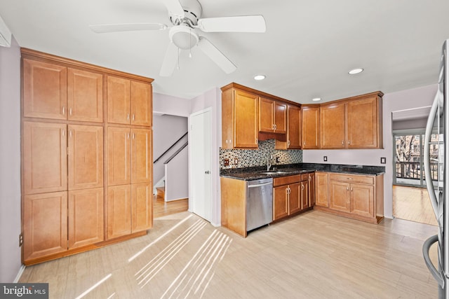 kitchen featuring appliances with stainless steel finishes, tasteful backsplash, sink, dark stone counters, and light wood-type flooring