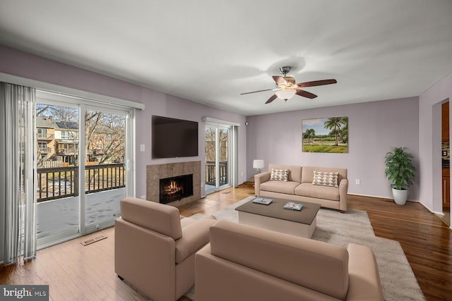 living room featuring a tile fireplace, ceiling fan, and light wood-type flooring