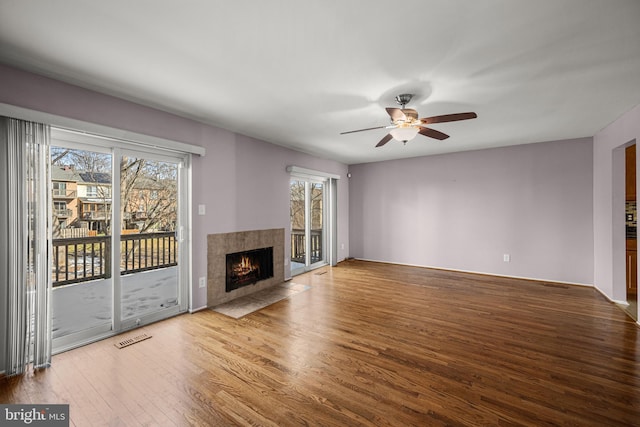 unfurnished living room with hardwood / wood-style flooring, a tiled fireplace, plenty of natural light, and ceiling fan