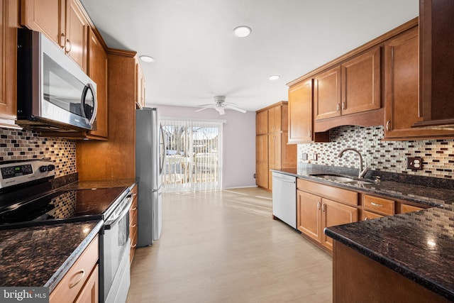 kitchen with sink, ceiling fan, dark stone countertops, backsplash, and stainless steel appliances