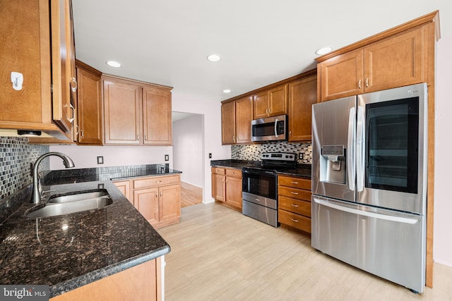 kitchen featuring appliances with stainless steel finishes, tasteful backsplash, sink, dark stone countertops, and light hardwood / wood-style floors