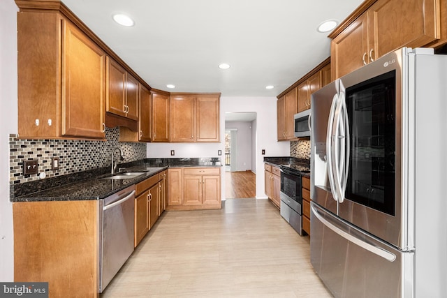 kitchen featuring sink, light hardwood / wood-style flooring, dark stone countertops, appliances with stainless steel finishes, and backsplash