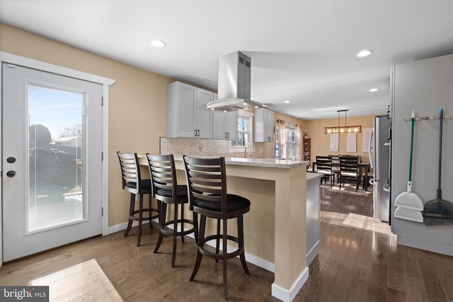 kitchen featuring stainless steel fridge, a breakfast bar, white cabinetry, island exhaust hood, and kitchen peninsula