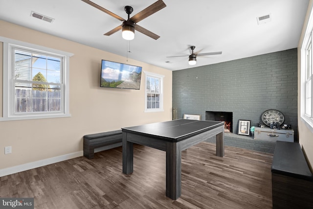 playroom featuring brick wall, a brick fireplace, dark hardwood / wood-style floors, and ceiling fan