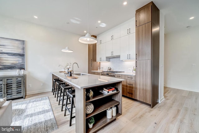 kitchen with pendant lighting, sink, backsplash, an island with sink, and white cabinets