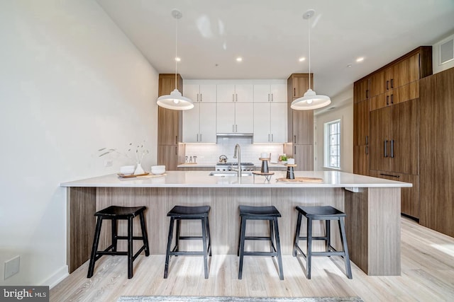 kitchen featuring backsplash, a breakfast bar, hanging light fixtures, and white cabinets