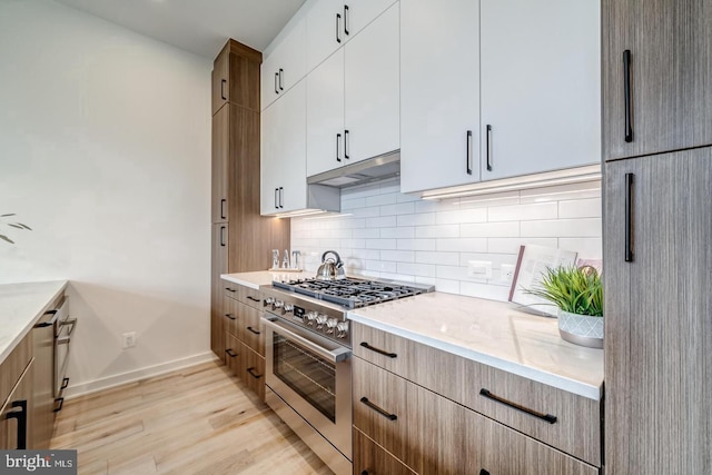 kitchen with white cabinets, stainless steel stove, backsplash, and light hardwood / wood-style floors