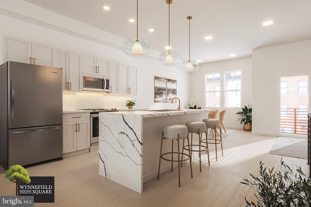 kitchen featuring decorative light fixtures, white cabinetry, stainless steel appliances, light stone countertops, and a center island with sink