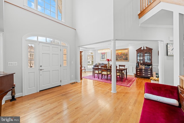 foyer with hardwood / wood-style flooring, a towering ceiling, and ornate columns