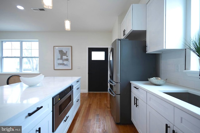 kitchen with dark wood-type flooring, stainless steel appliances, decorative backsplash, white cabinets, and decorative light fixtures