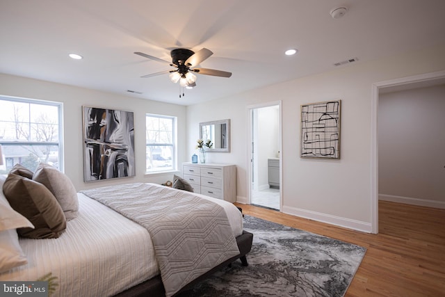 bedroom with multiple windows, wood-type flooring, ceiling fan, and ensuite bath