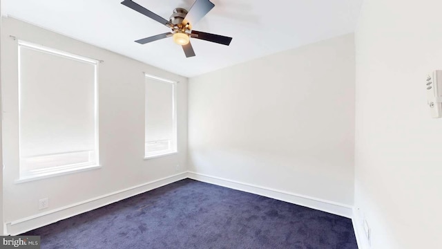 spare room with dark carpet, a ceiling fan, and baseboards