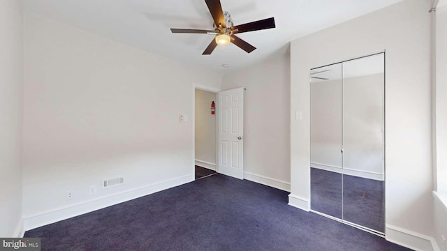 unfurnished bedroom featuring dark colored carpet, a closet, visible vents, a ceiling fan, and baseboards