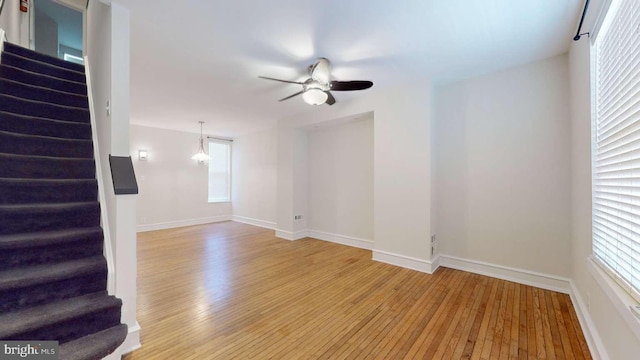 unfurnished living room featuring a ceiling fan, light wood-style flooring, baseboards, and stairs