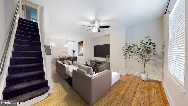 living room with a ceiling fan, light wood-type flooring, baseboards, and stairs