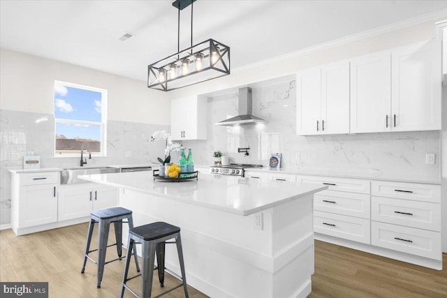 kitchen with wall chimney range hood, sink, white cabinetry, stove, and a center island