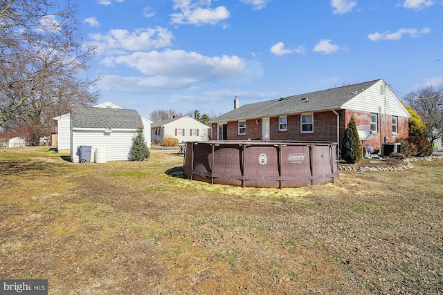 back of property with an outbuilding, central AC, brick siding, a yard, and an outdoor pool