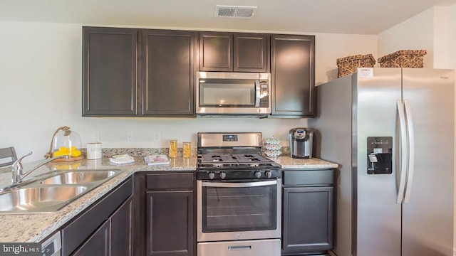 kitchen with stainless steel appliances, light stone countertops, sink, and dark brown cabinets