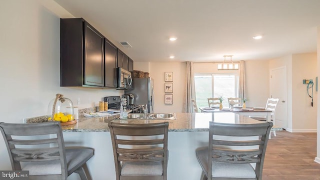 kitchen with stainless steel appliances, a breakfast bar area, light stone counters, and light hardwood / wood-style floors