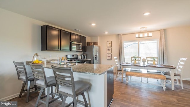 kitchen featuring a breakfast bar, appliances with stainless steel finishes, light stone countertops, light hardwood / wood-style floors, and kitchen peninsula