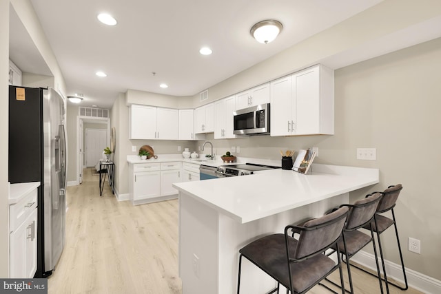 kitchen featuring stainless steel appliances, light countertops, white cabinetry, and a peninsula