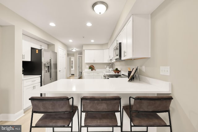 kitchen with a breakfast bar area, a peninsula, white cabinets, light countertops, and appliances with stainless steel finishes