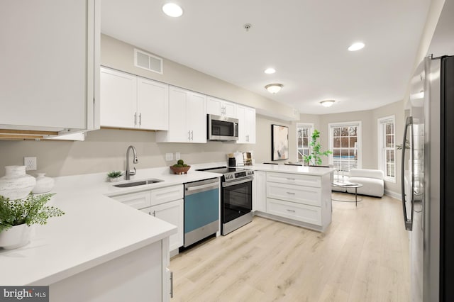 kitchen with visible vents, appliances with stainless steel finishes, a peninsula, light countertops, and a sink