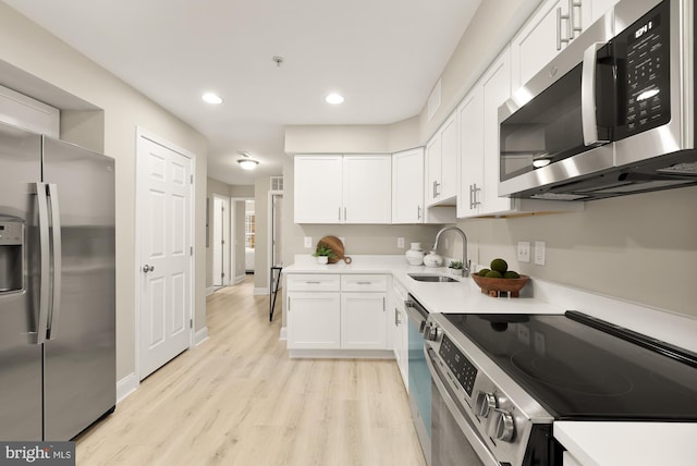 kitchen featuring light wood-style flooring, stainless steel appliances, light countertops, white cabinetry, and a sink