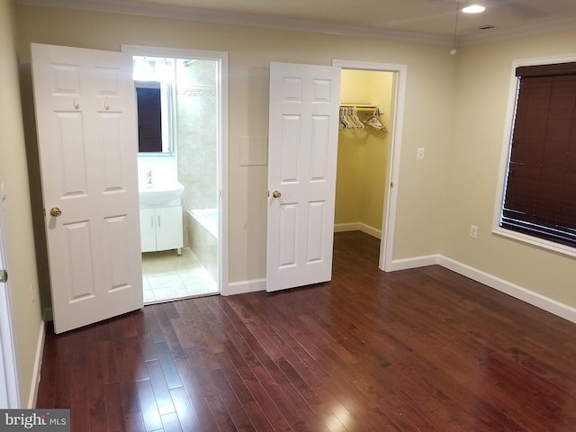 unfurnished bedroom featuring ornamental molding, a walk in closet, dark wood-style flooring, and baseboards