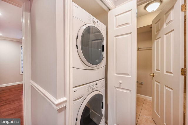 laundry area featuring stacked washer and dryer, laundry area, light tile patterned flooring, and baseboards