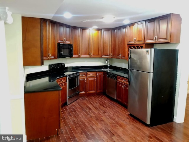 kitchen with stainless steel appliances, dark countertops, dark wood-style flooring, and a sink