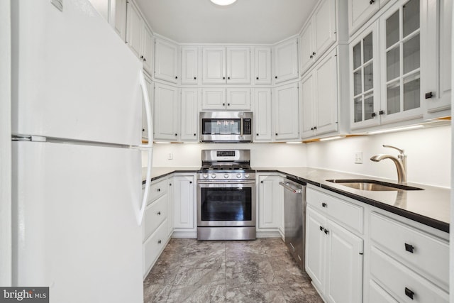 kitchen featuring a sink, white cabinets, appliances with stainless steel finishes, dark countertops, and glass insert cabinets