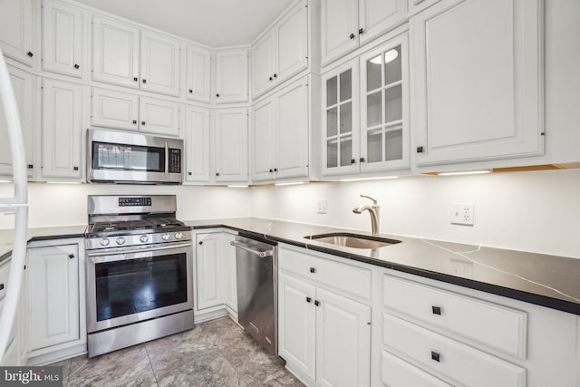 kitchen featuring dark countertops, glass insert cabinets, stainless steel appliances, white cabinetry, and a sink