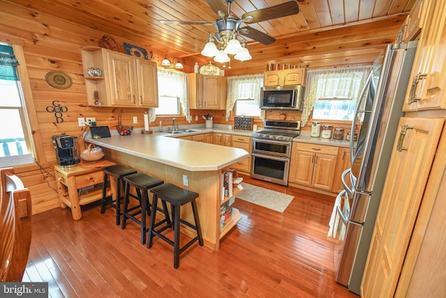 kitchen featuring a breakfast bar area, wood ceiling, appliances with stainless steel finishes, wooden walls, and kitchen peninsula