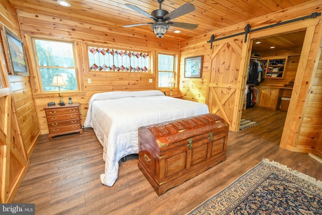 bedroom featuring dark wood-type flooring, wooden ceiling, a barn door, and wooden walls