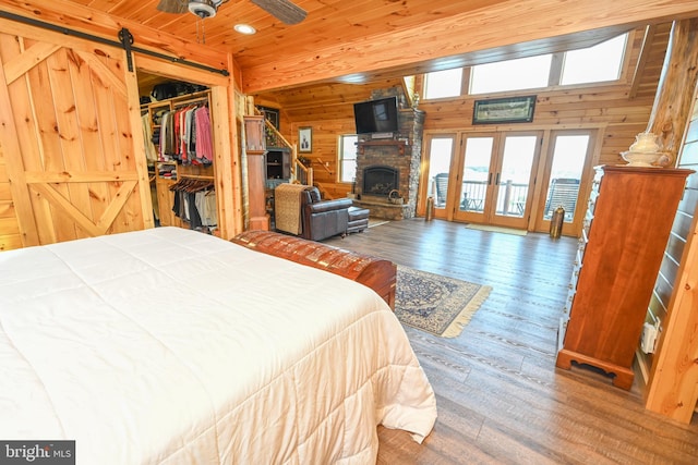 bedroom with wooden walls, a fireplace, hardwood / wood-style flooring, a barn door, and wooden ceiling