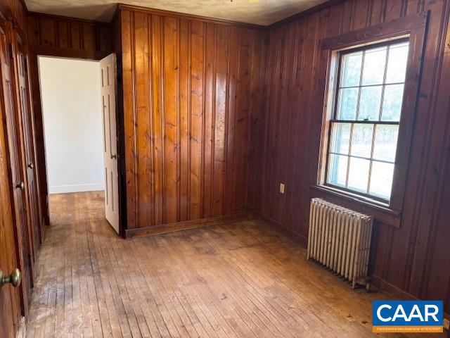 empty room with radiator heating unit, wooden walls, and light hardwood / wood-style floors