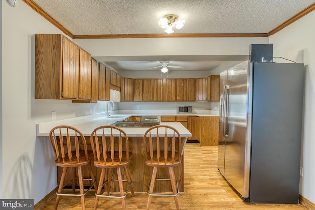 kitchen featuring crown molding, brown cabinetry, a peninsula, and stainless steel appliances