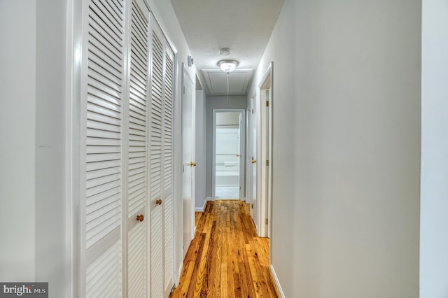 corridor featuring baseboards, light wood finished floors, and attic access