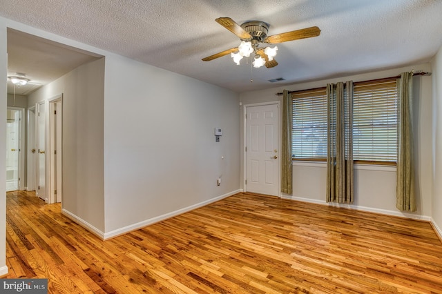 spare room featuring light wood finished floors, visible vents, a textured ceiling, and ceiling fan