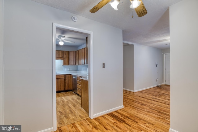 kitchen with dishwasher, light countertops, ceiling fan, light wood-style floors, and brown cabinetry