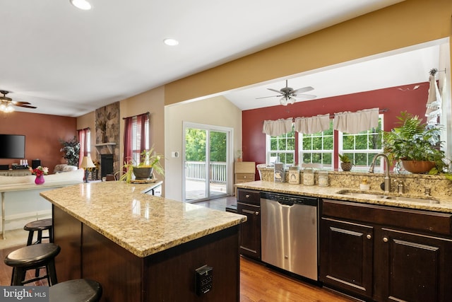 kitchen featuring dark brown cabinetry, sink, stainless steel dishwasher, a kitchen breakfast bar, and light stone countertops