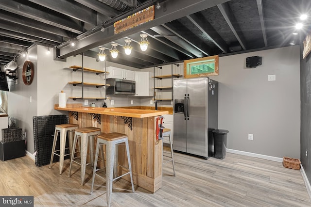 kitchen featuring appliances with stainless steel finishes, a breakfast bar, white cabinetry, butcher block counters, and light wood-type flooring